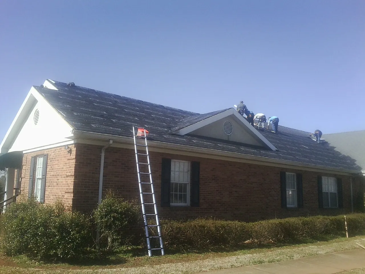 Crew tearing shingles off a brick ranch roof with a ladder set — Emergency Roof Repair work by our crew in Center Line