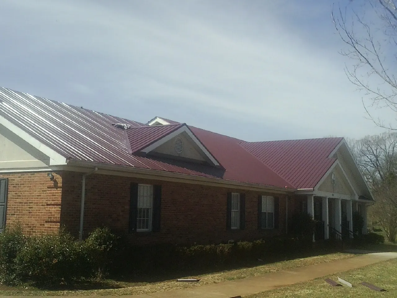 Red metal roof with gabled entries on a long brick building, from a Hail Damage Roof Repair job in Center Line
