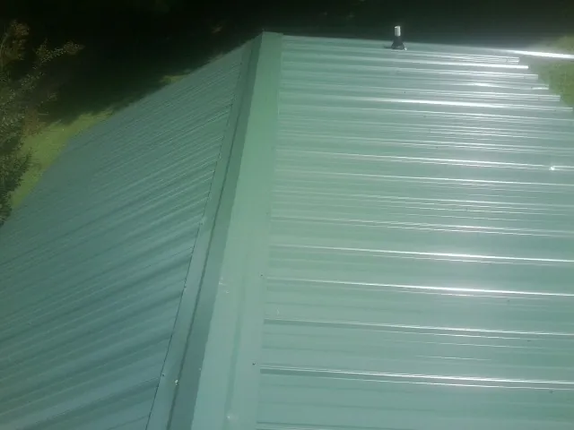 New green metal panels meeting at the ridge of a roof — Flat Roof Repair work by our crew in Center Line