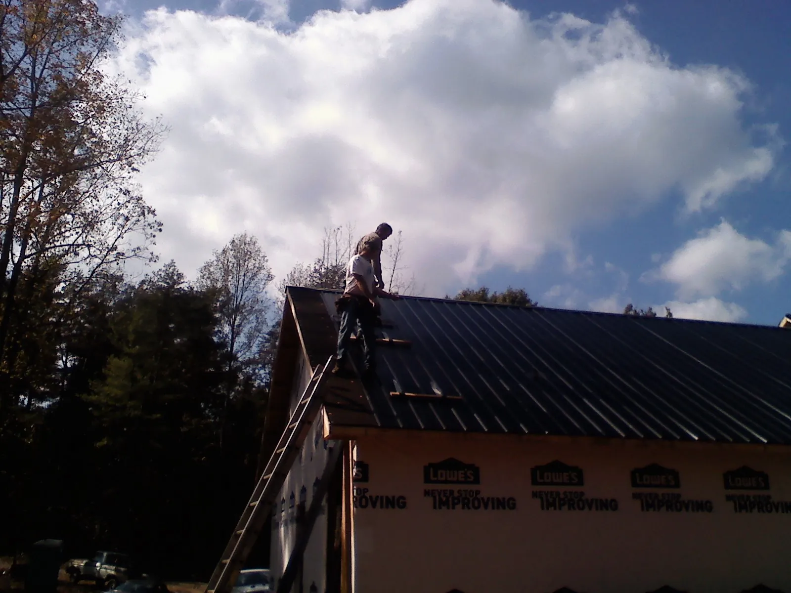 Roofer fastening dark metal panels high against a cloudy sky, from a Roof Inspection job in Center Line