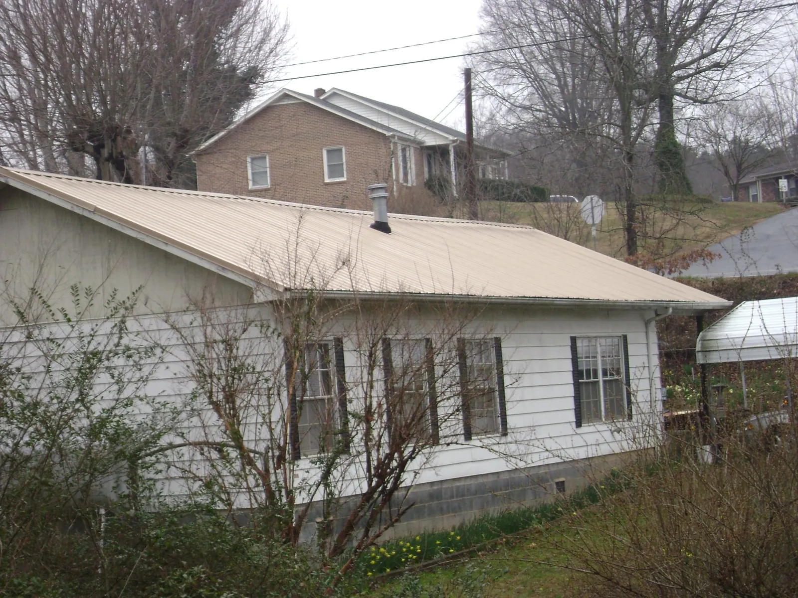 Tan metal roof on a white sided house set into a hillside — Commercial Roofing by Roofing Brothers in Center Line