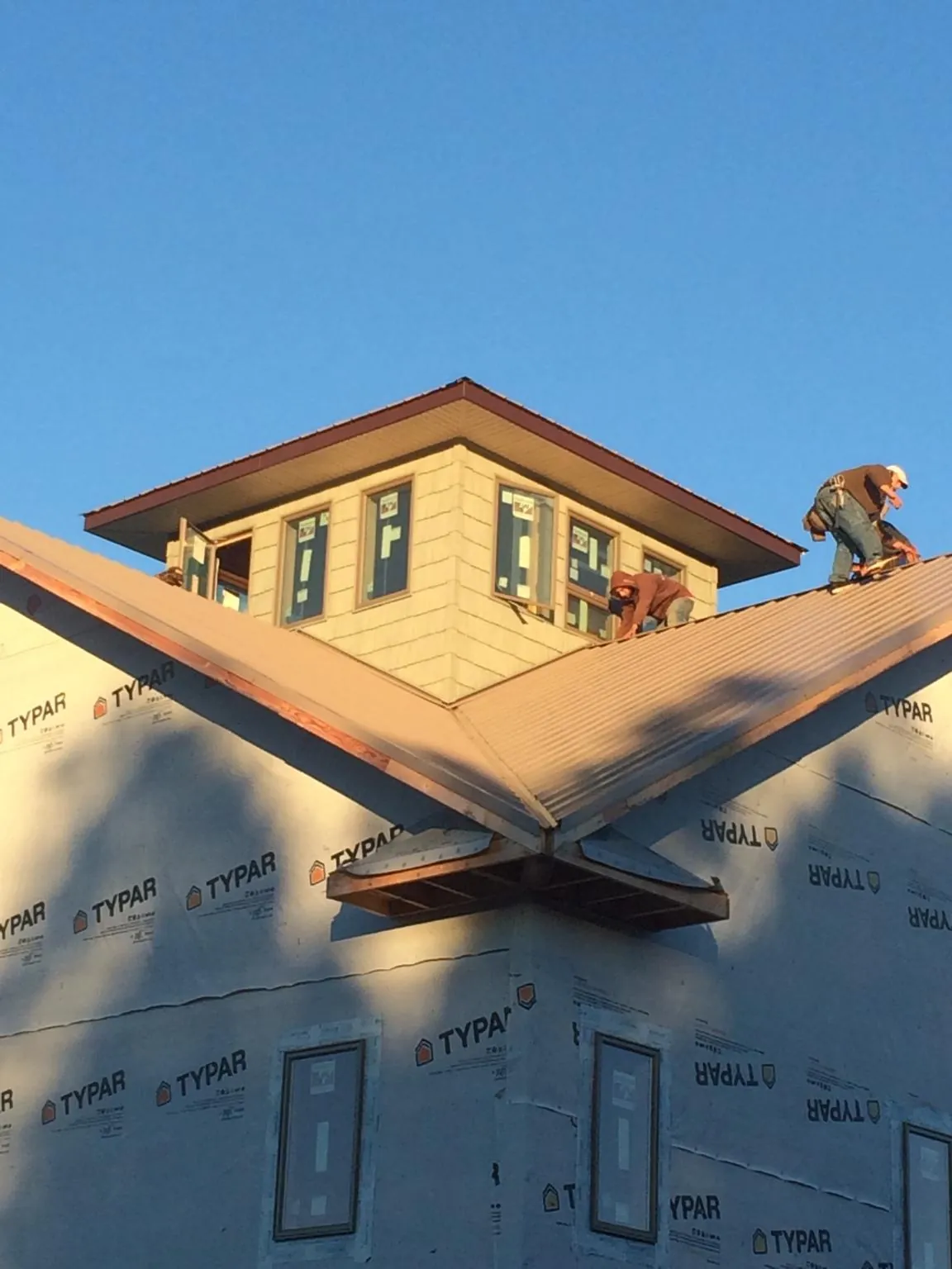 Roofers working around a rooftop cupola on a new metal roof at sunset — Roof Waterproofing in Center Line by Roofing Brothers